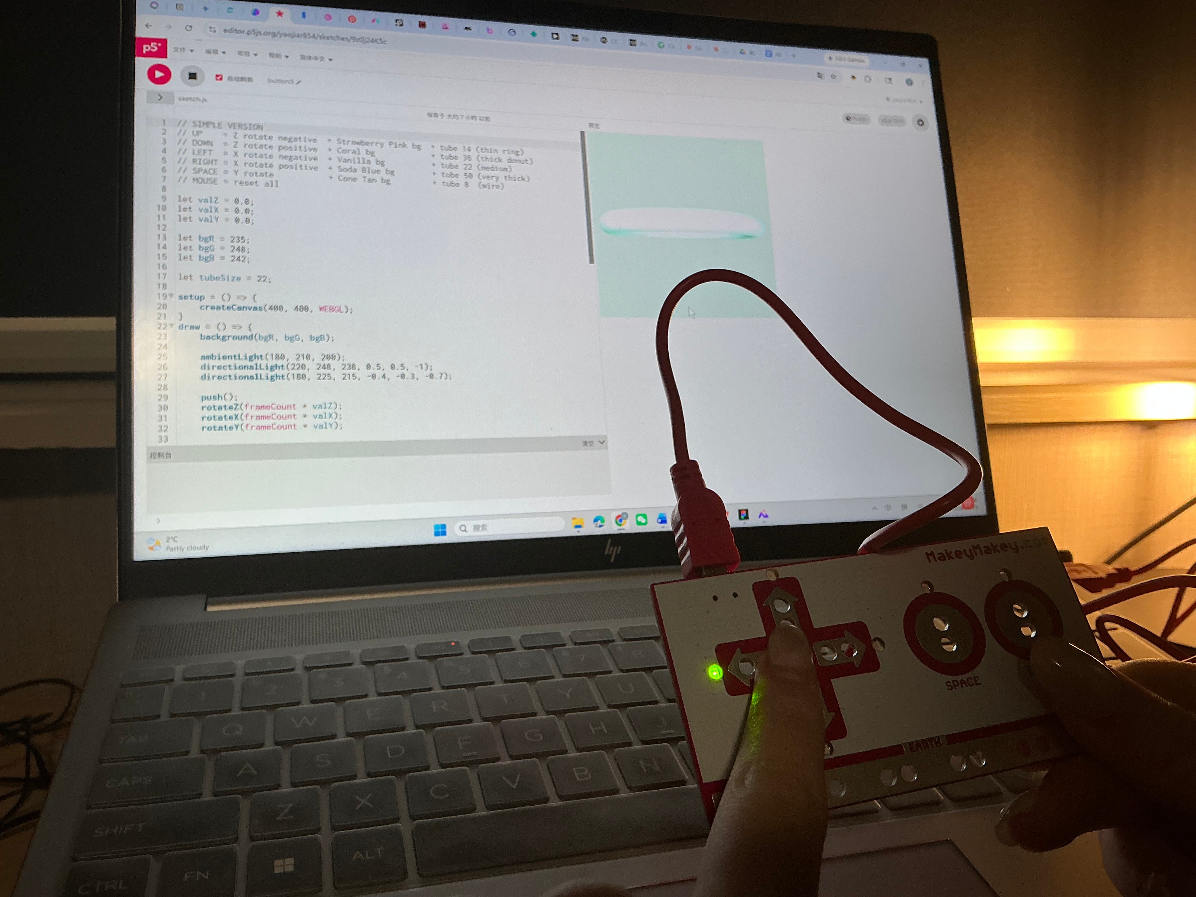 Hand holds Makey Makey as the laptop displays a white flat card shape rotating in 3D space.