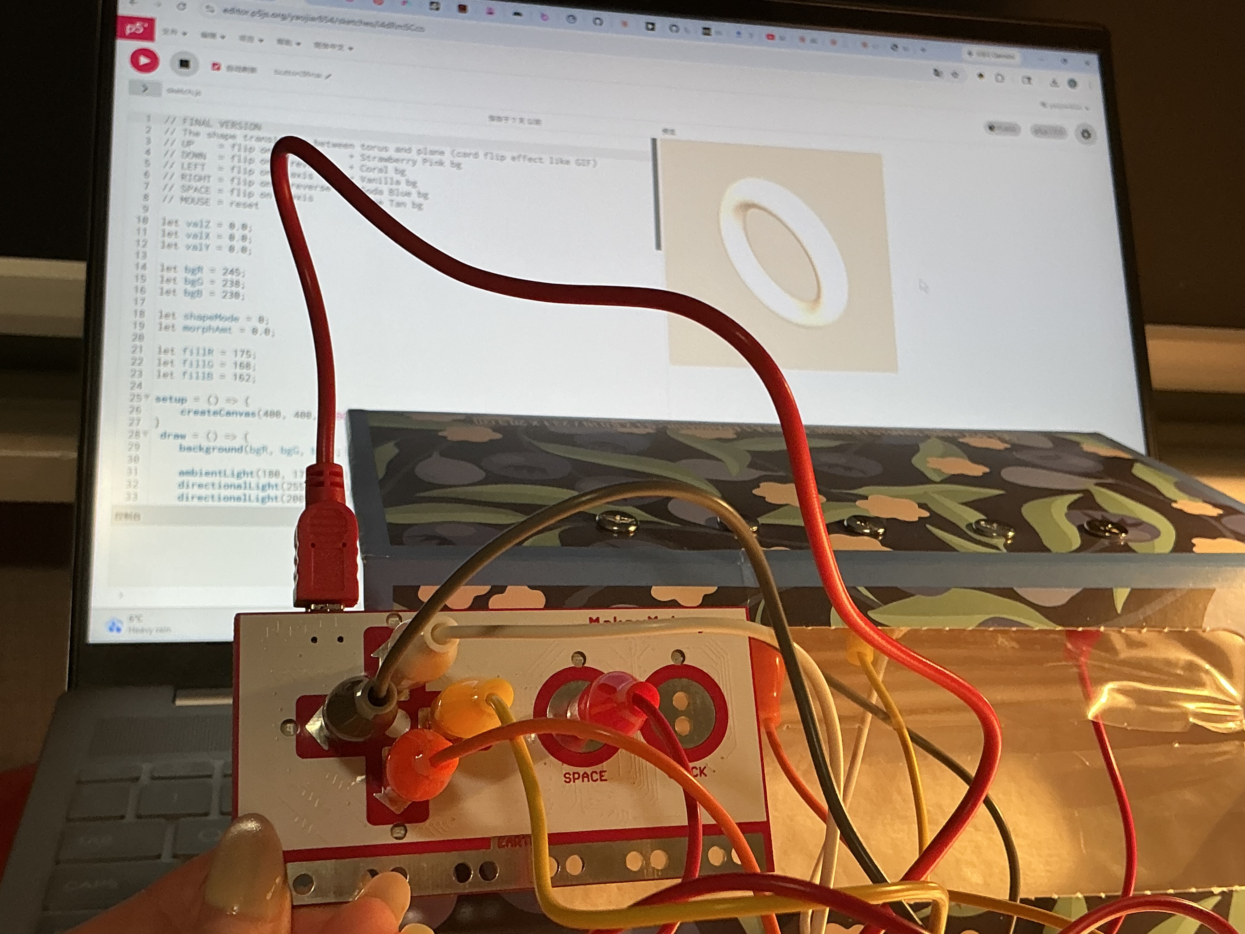 The image displays a laptop screen showing a white 3D torus ring shape with the Makey Makey and wired interface beside it, confirming the iron wire loops are triggering the sketch correctly.